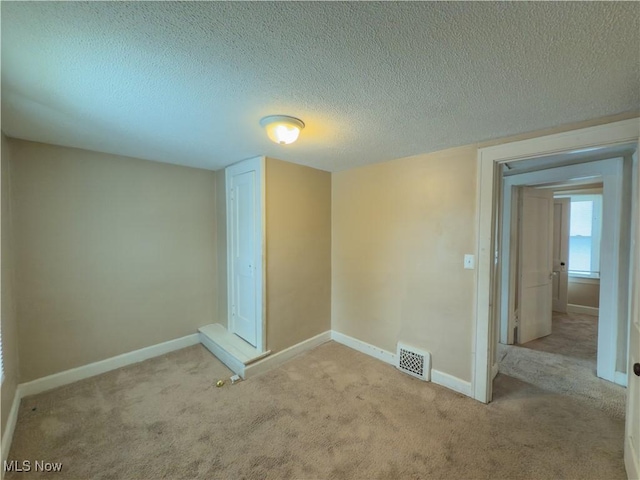 spare room featuring light carpet, visible vents, a textured ceiling, and baseboards