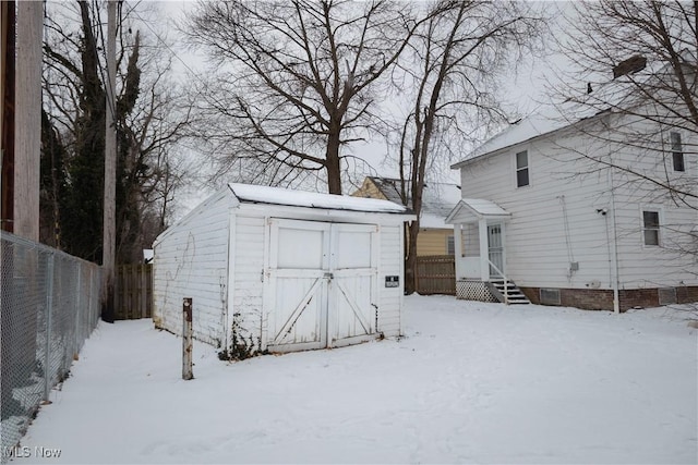 snow covered structure featuring an outbuilding, fence, and a shed