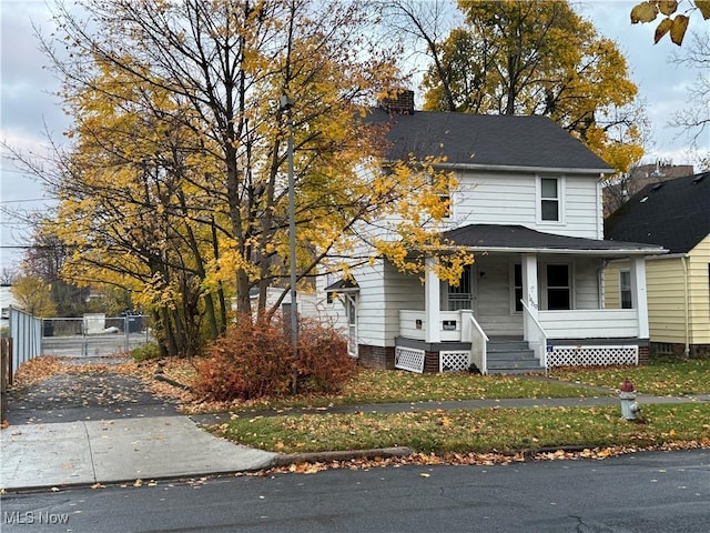 view of front facade with covered porch, a front lawn, a chimney, and fence