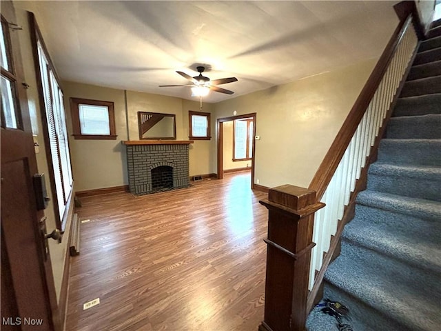 unfurnished living room with hardwood / wood-style flooring, ceiling fan, and a brick fireplace