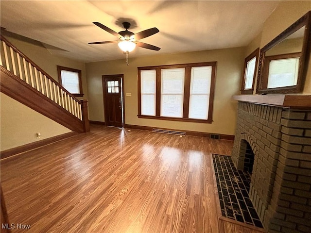 unfurnished living room with a fireplace, a wealth of natural light, wood-type flooring, and ceiling fan