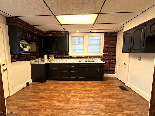 bar with sink, a paneled ceiling, light hardwood / wood-style floors, and brick wall