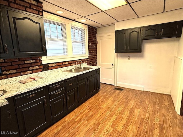 kitchen featuring sink, light hardwood / wood-style flooring, light stone counters, brick wall, and a drop ceiling