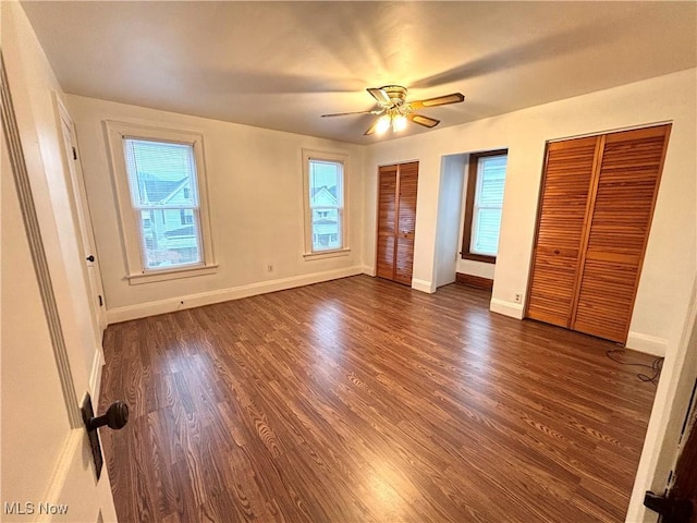 unfurnished bedroom featuring ceiling fan, two closets, and dark hardwood / wood-style flooring