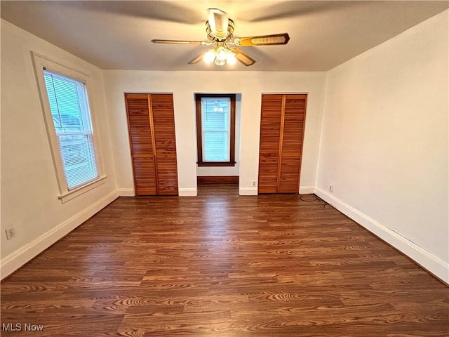 unfurnished bedroom featuring multiple windows, ceiling fan, dark hardwood / wood-style floors, and multiple closets