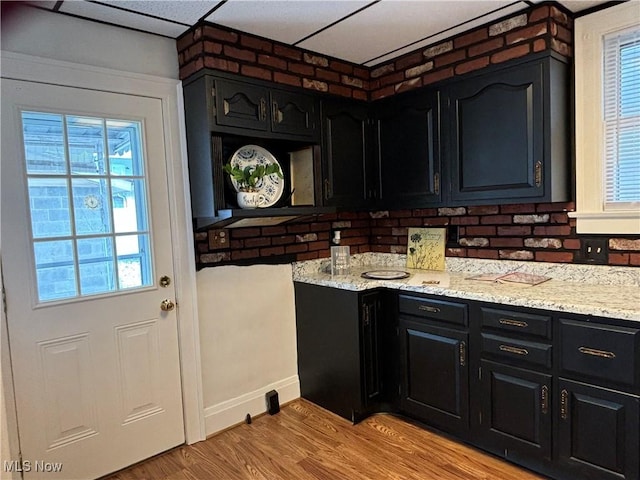 kitchen featuring brick wall, light stone countertops, and light wood-type flooring