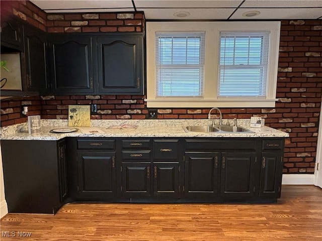 kitchen featuring a paneled ceiling, brick wall, sink, and light hardwood / wood-style flooring