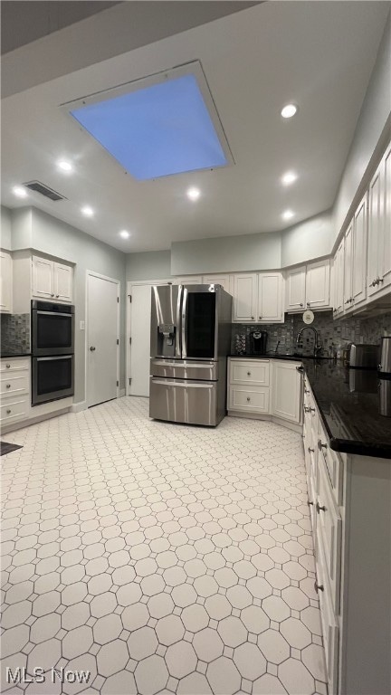 kitchen featuring white cabinets, black double oven, a skylight, decorative backsplash, and stainless steel fridge