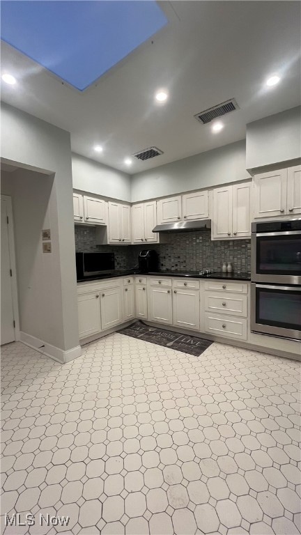 kitchen with decorative backsplash, white cabinets, and appliances with stainless steel finishes