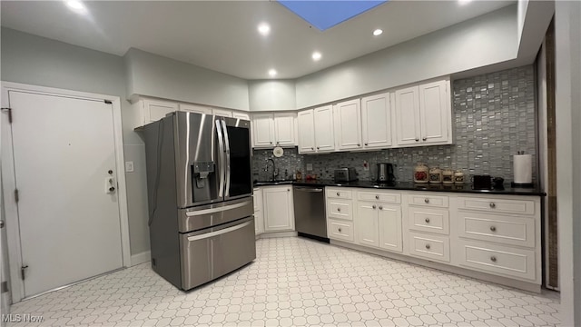 kitchen featuring a skylight, white cabinetry, sink, stainless steel appliances, and tasteful backsplash