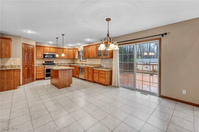 kitchen with brown cabinetry, baseboards, a kitchen island, stainless steel appliances, and backsplash