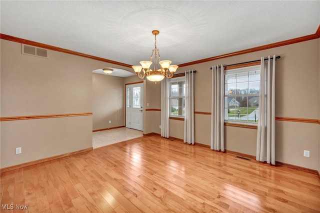 empty room featuring a chandelier, light hardwood / wood-style flooring, a healthy amount of sunlight, and ornamental molding