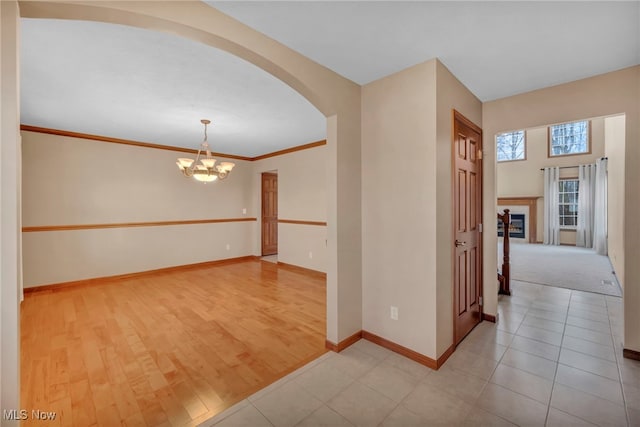 interior space featuring baseboards, an inviting chandelier, light wood-style flooring, arched walkways, and ornamental molding