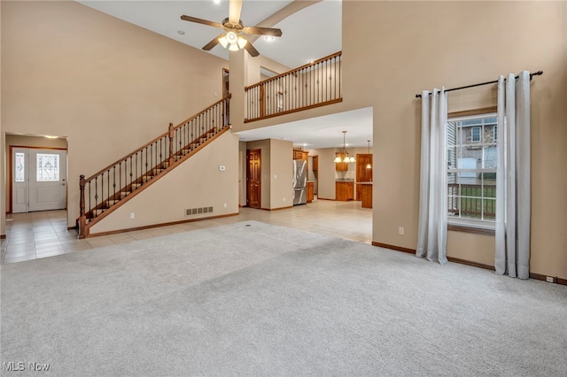 unfurnished living room with ceiling fan with notable chandelier, a healthy amount of sunlight, light carpet, and a high ceiling