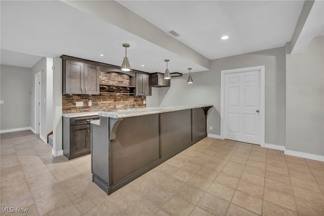 kitchen featuring pendant lighting, dark brown cabinets, light stone counters, and decorative backsplash