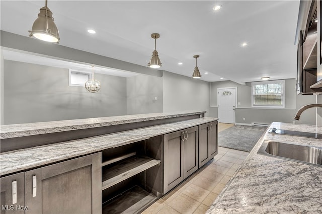 kitchen featuring decorative light fixtures, light stone counters, dark brown cabinetry, and sink