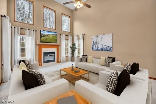 living room with a high ceiling, a healthy amount of sunlight, a glass covered fireplace, and a ceiling fan
