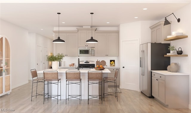 kitchen with appliances with stainless steel finishes, light wood-type flooring, decorative light fixtures, a center island with sink, and a breakfast bar area