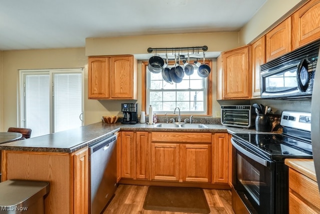 kitchen with black appliances, kitchen peninsula, sink, and light hardwood / wood-style flooring