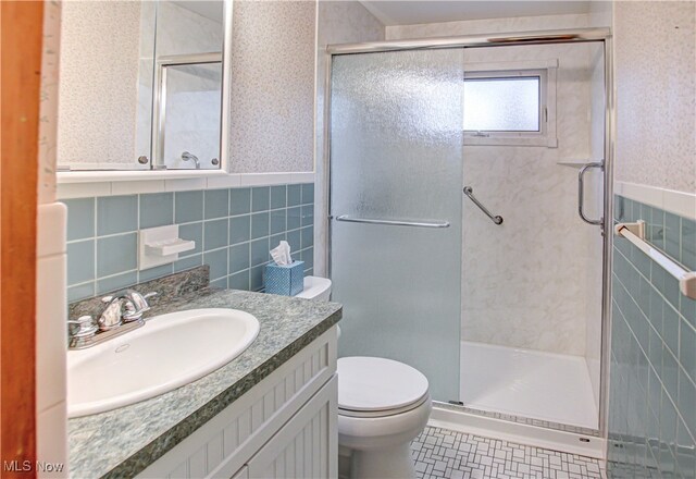 bathroom with tile patterned floors, vanity, a shower with door, tile walls, and toilet