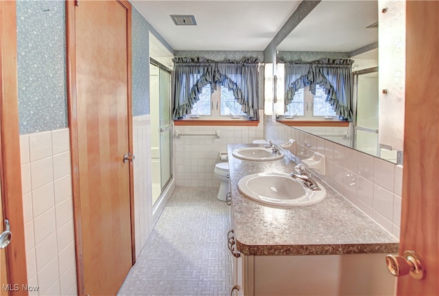 bathroom with tile patterned floors, vanity, a shower with door, tile walls, and toilet