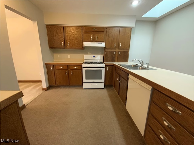 kitchen featuring white appliances, light carpet, sink, a skylight, and kitchen peninsula