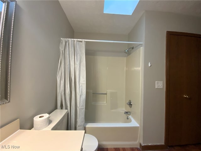 full bathroom with a skylight, hardwood / wood-style floors, toilet, shower / tub combo with curtain, and vanity