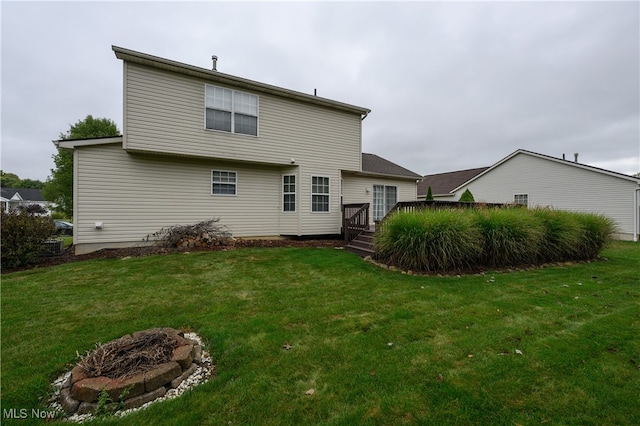 back of property with a yard, a fire pit, and a deck