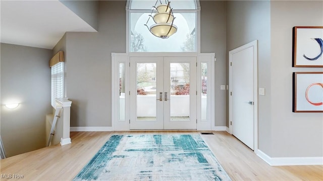 doorway to outside with light wood-type flooring, a high ceiling, and french doors