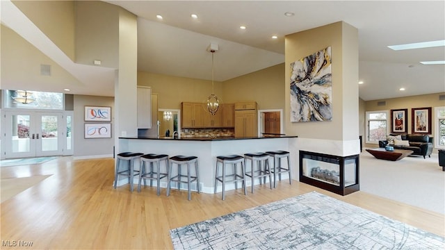 kitchen with kitchen peninsula, decorative backsplash, a kitchen bar, pendant lighting, and high vaulted ceiling