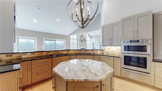 kitchen with a center island, sink, vaulted ceiling, light stone countertops, and appliances with stainless steel finishes