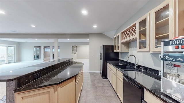 kitchen featuring stainless steel dishwasher, black refrigerator, dark stone countertops, and sink