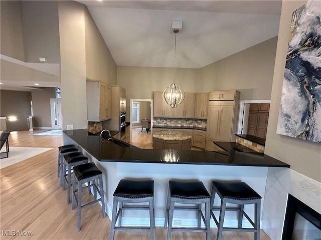 kitchen with backsplash, high vaulted ceiling, hanging light fixtures, a kitchen bar, and kitchen peninsula