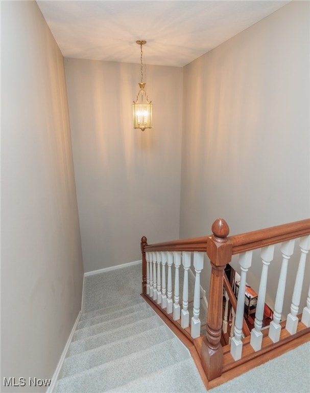 stairs with carpet floors and an inviting chandelier