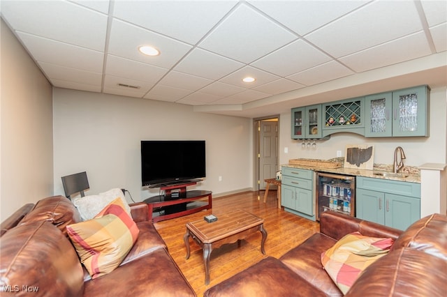 living room with a drop ceiling, light hardwood / wood-style flooring, wet bar, and beverage cooler