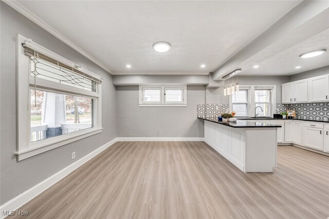 kitchen with kitchen peninsula, tasteful backsplash, ornamental molding, light hardwood / wood-style flooring, and white cabinets