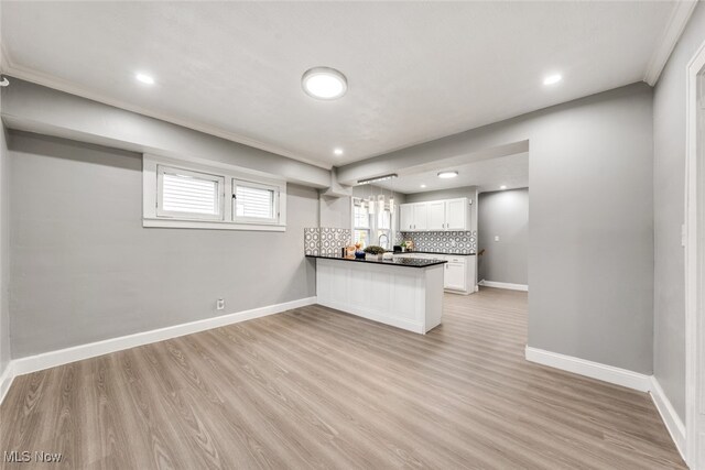 kitchen with decorative backsplash, kitchen peninsula, crown molding, white cabinets, and light hardwood / wood-style floors