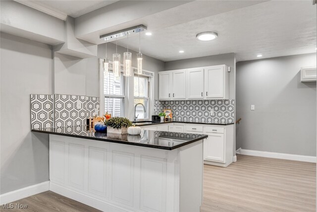 kitchen featuring sink, kitchen peninsula, hanging light fixtures, decorative backsplash, and white cabinetry