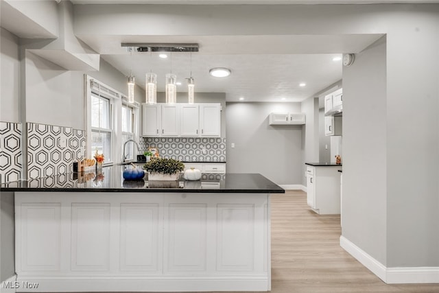 kitchen featuring white cabinets, light wood-type flooring, kitchen peninsula, and hanging light fixtures