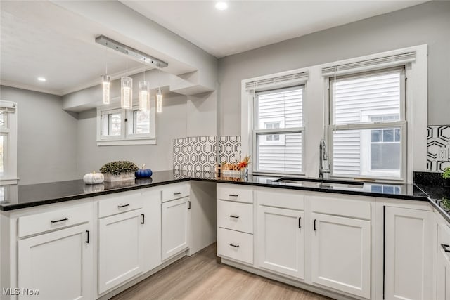 kitchen with kitchen peninsula, sink, light hardwood / wood-style floors, white cabinetry, and hanging light fixtures