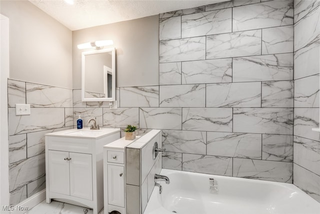 bathroom featuring vanity, a textured ceiling, a bathtub, and tile walls