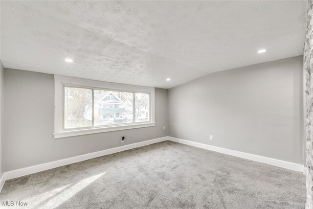 spare room featuring vaulted ceiling, carpet, and a textured ceiling