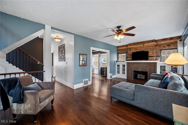 living room featuring wooden walls, dark hardwood / wood-style floors, ceiling fan, a textured ceiling, and a fireplace