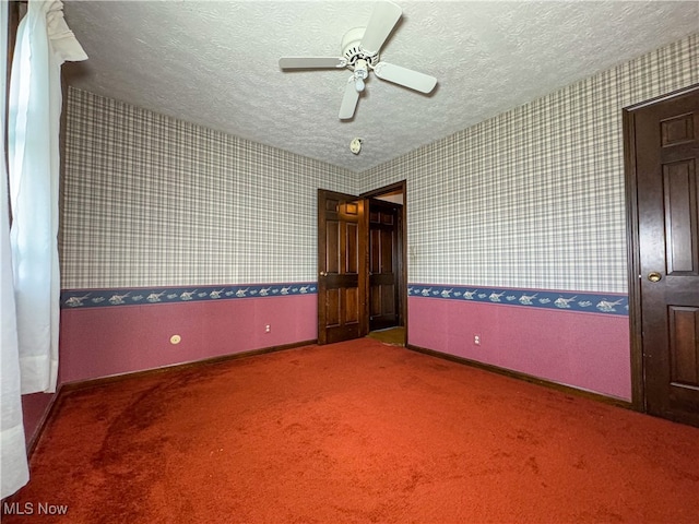 empty room featuring ceiling fan, a textured ceiling, and dark colored carpet