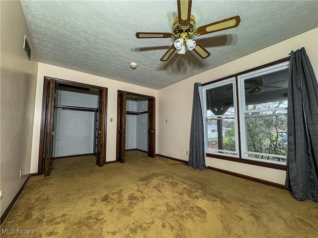 unfurnished bedroom featuring carpet flooring, a textured ceiling, two closets, and ceiling fan