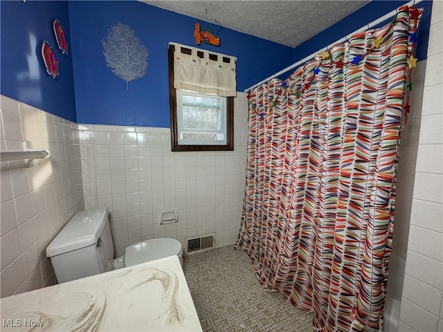 bathroom featuring curtained shower, tile patterned floors, a textured ceiling, toilet, and tile walls