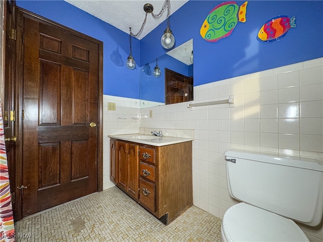 bathroom with a textured ceiling, vanity, toilet, and tile walls