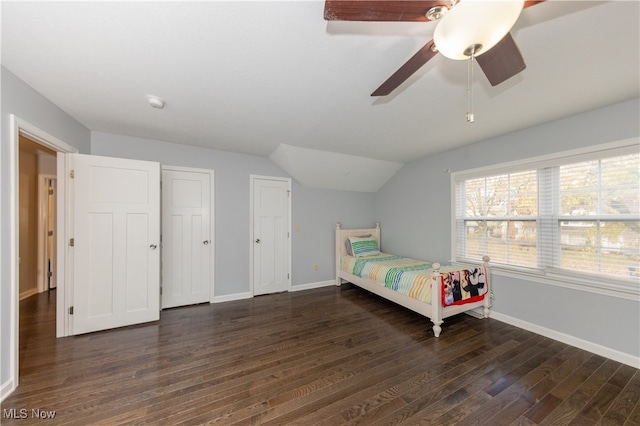 bedroom featuring dark hardwood / wood-style floors, vaulted ceiling, ceiling fan, and multiple closets