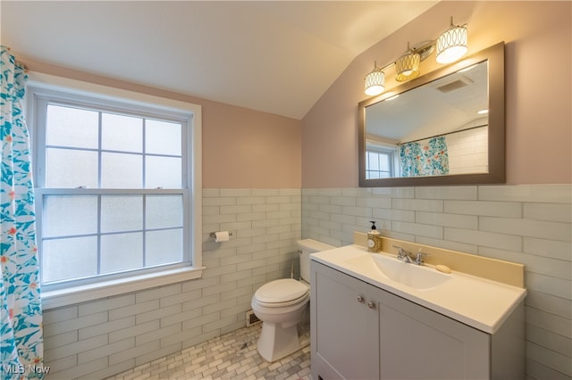 bathroom featuring vanity, lofted ceiling, tile patterned flooring, toilet, and tile walls