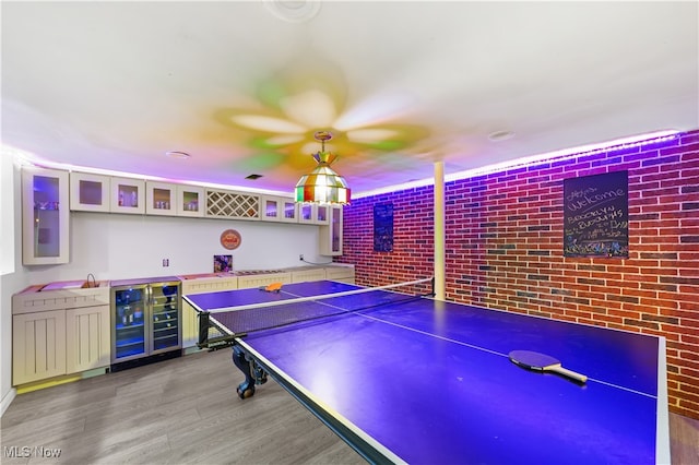 game room with wine cooler, hardwood / wood-style floors, brick wall, and indoor bar